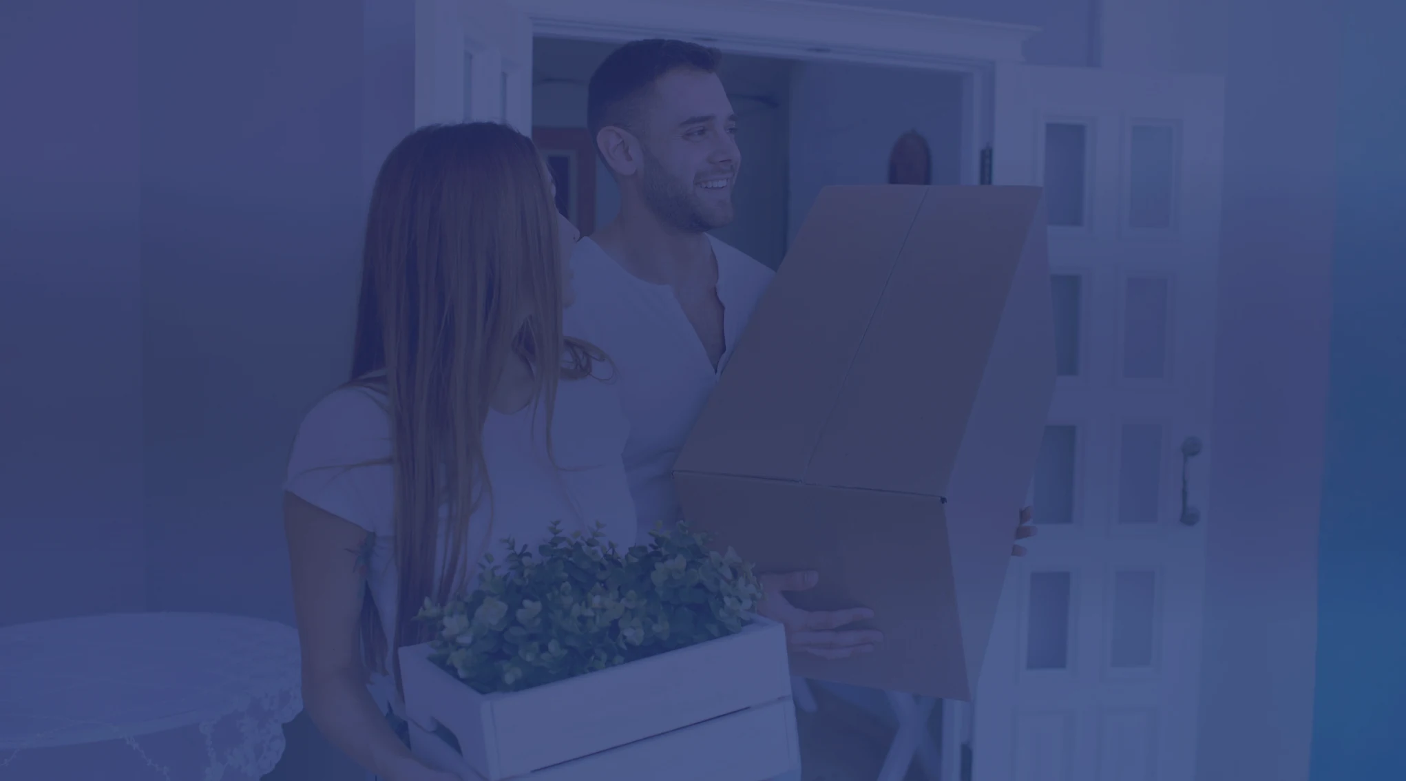 A couple carrying moving boxes through the front door of a new home
