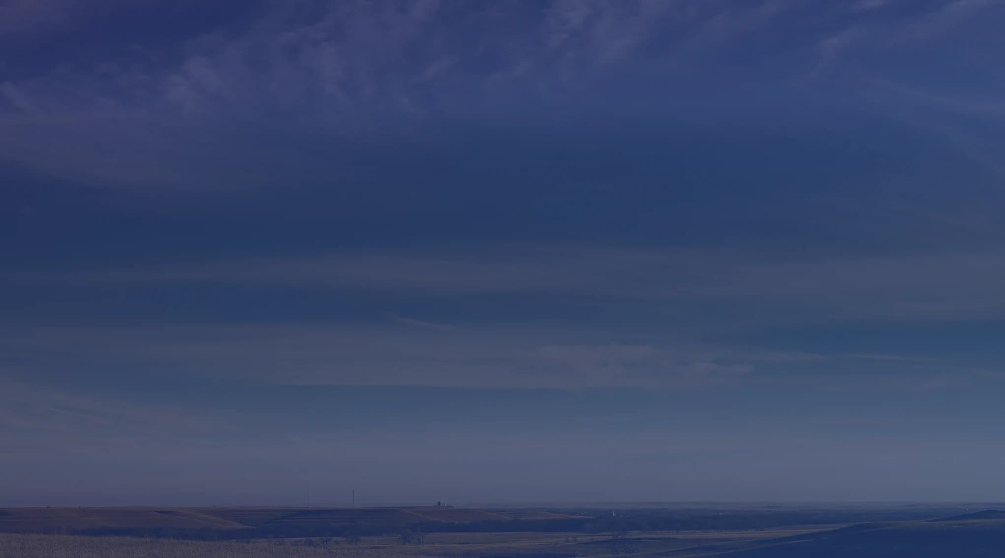 Rolling golden grassland stretches toward a low horizon under a broad blue sky streaked with wispy clouds.