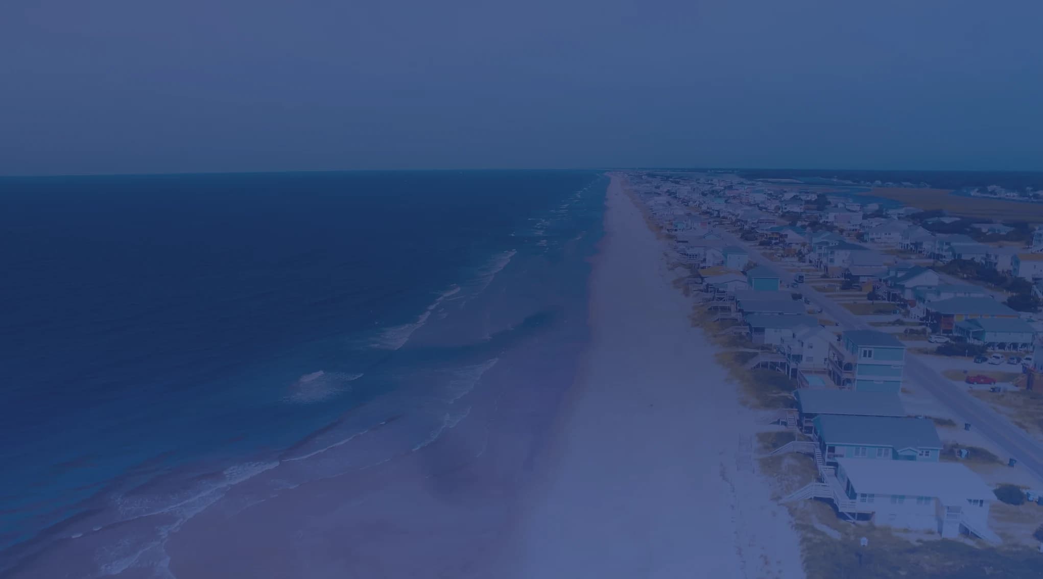 Aerial view of the North Carolina Crystal Coast shoreline, with teal Atlantic surf rolling onto pale sand, near MCAS Cherry Point and Havelock
