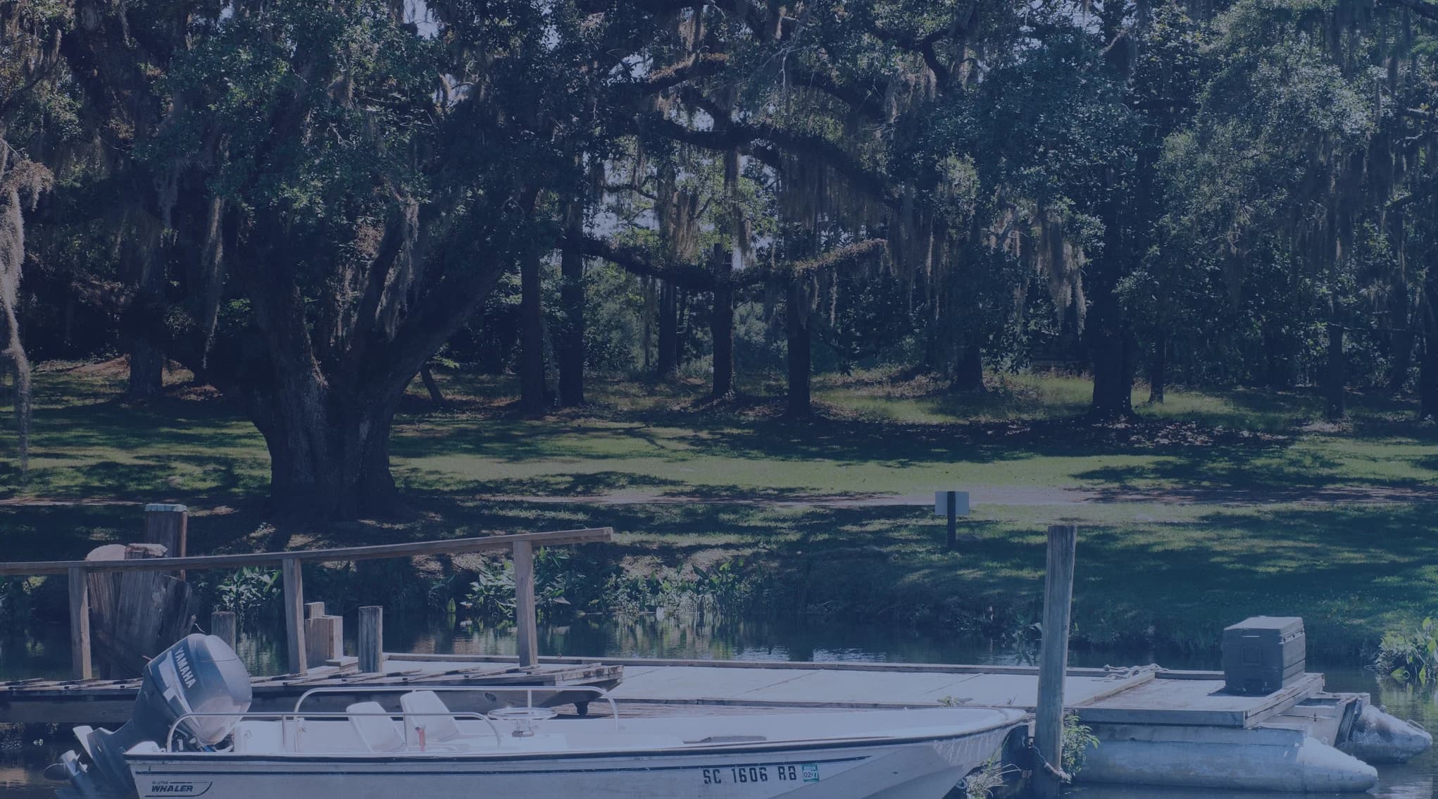 A small fishing boat moored at a wooden dock on a calm lake, surrounded by Spanish moss-draped live oaks in South Georgia