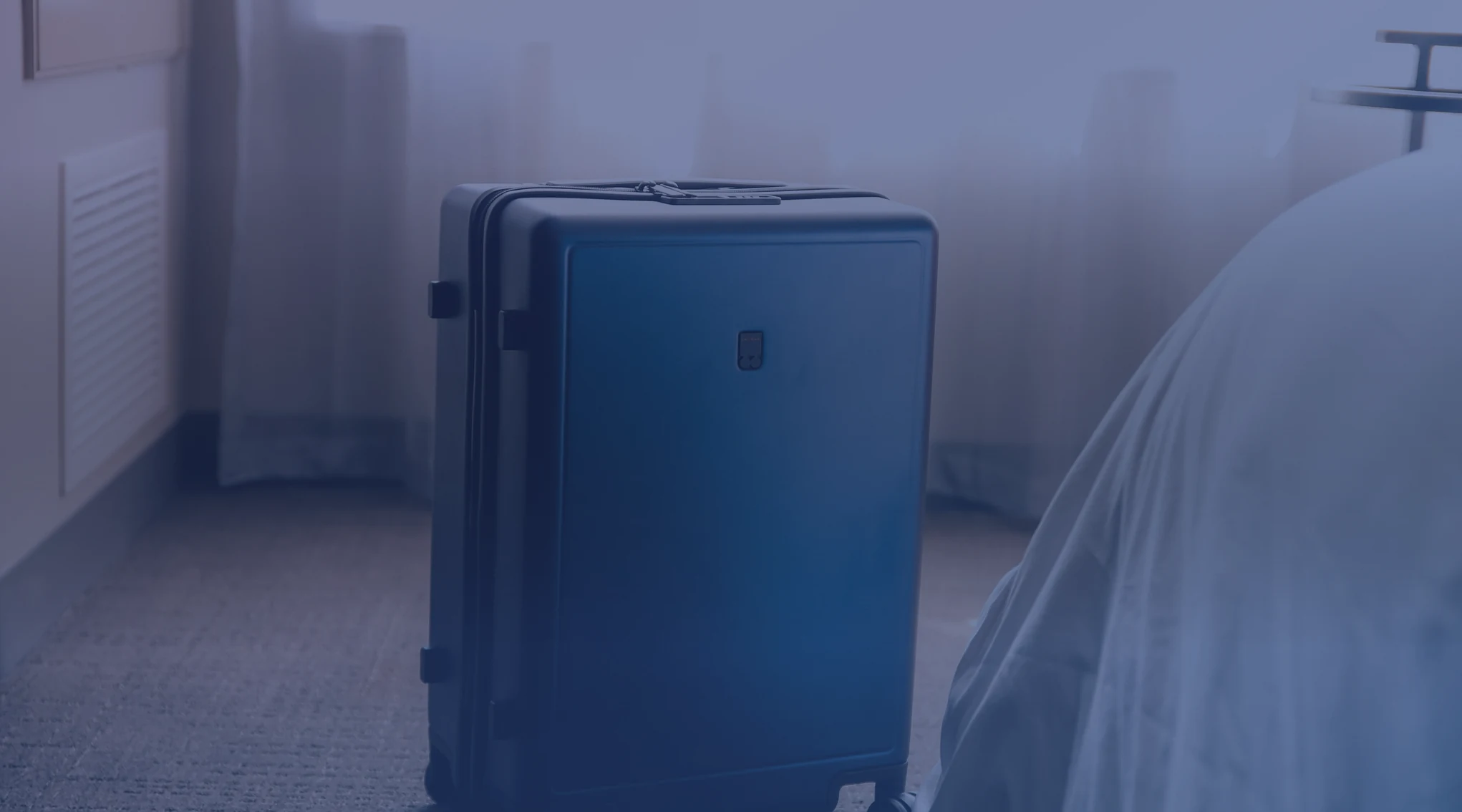A packed suitcase standing beside a bed in a temporary lodging room
