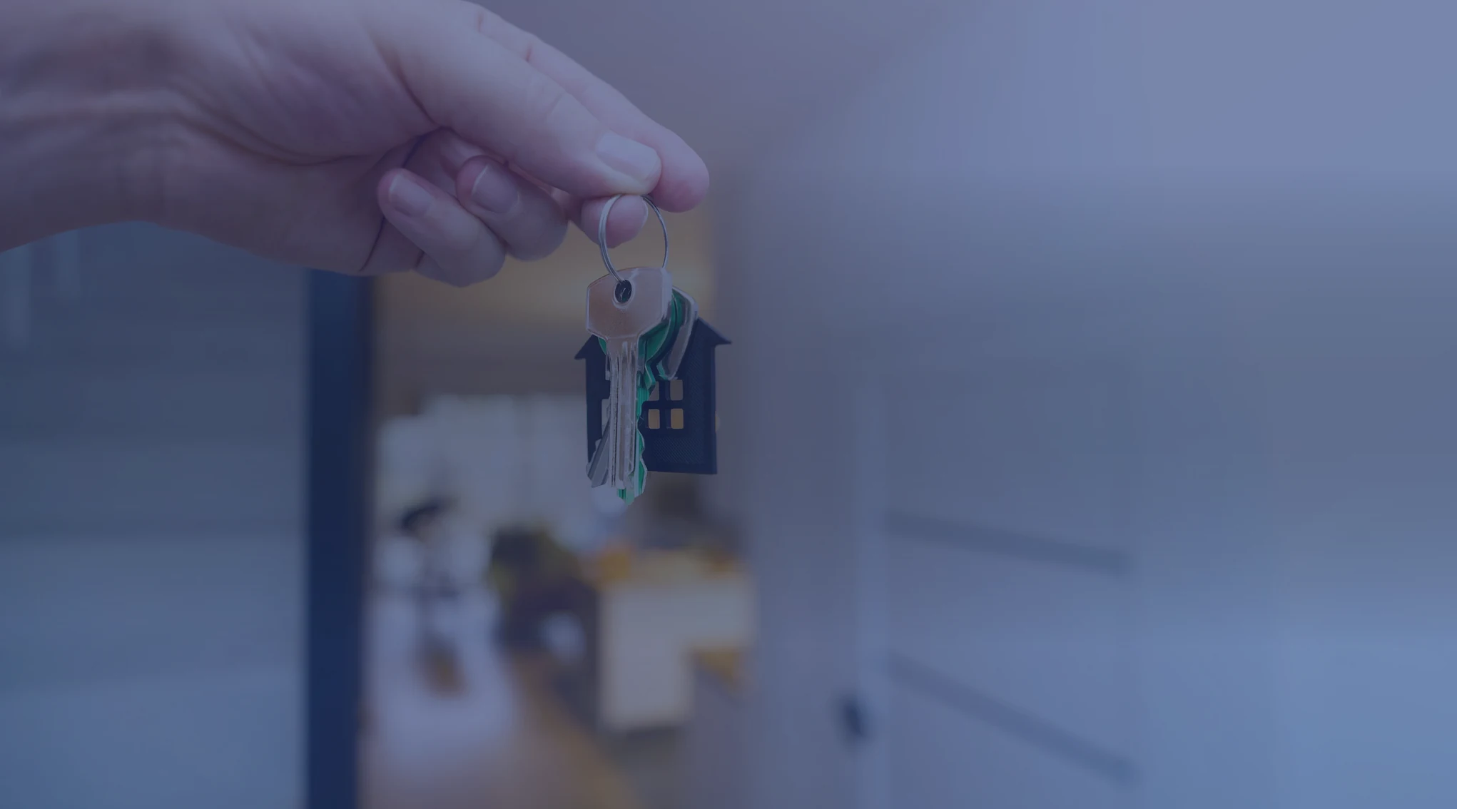 A hand holding a set of house keys in front of a home entrance