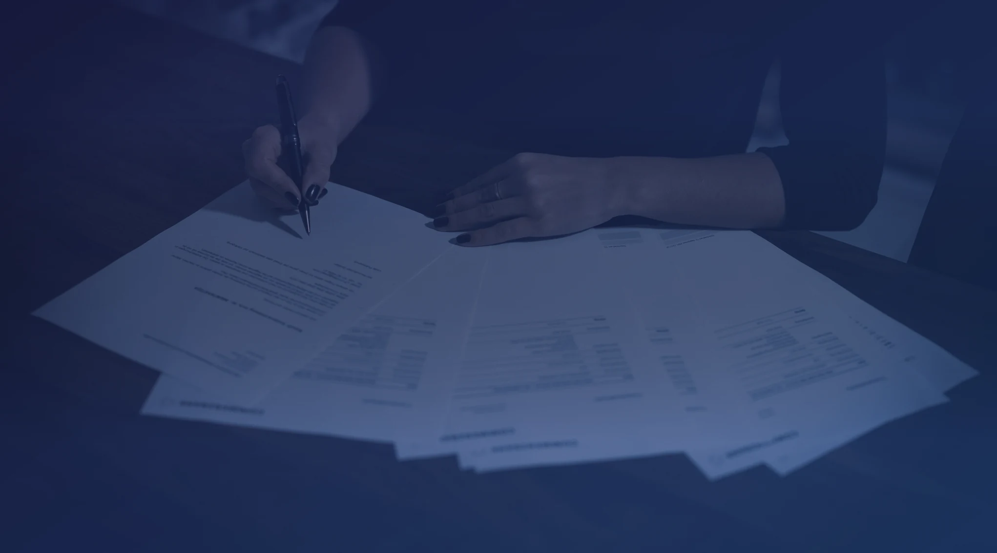 A woman seated at a table reviewing and signing a stack of documents