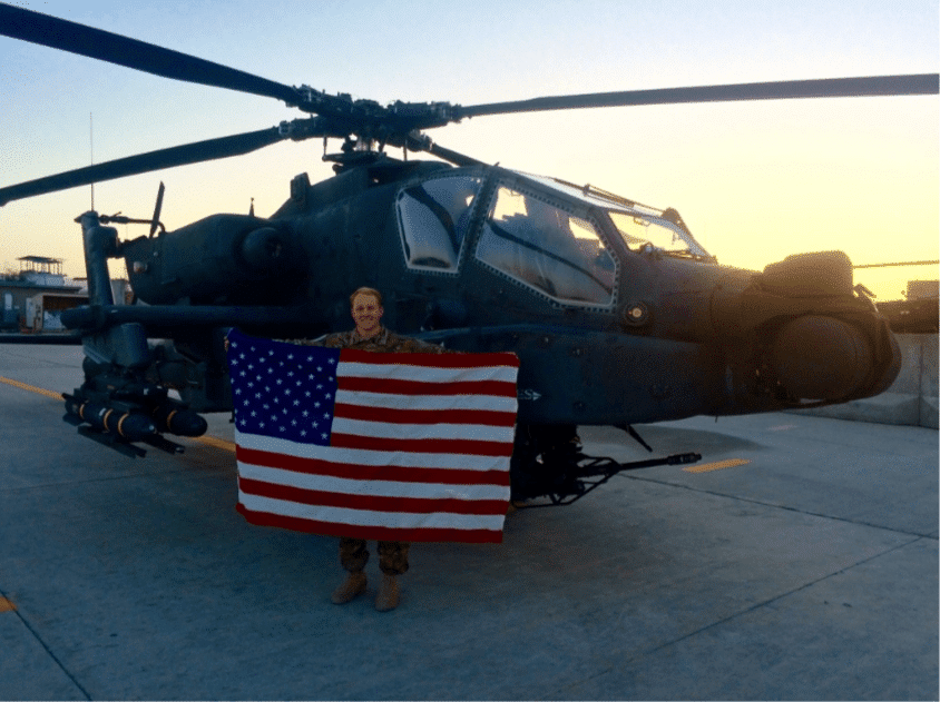 Founder & CEO Jason Anderson holding american Flag in front of AH--64D Apache Helicopter